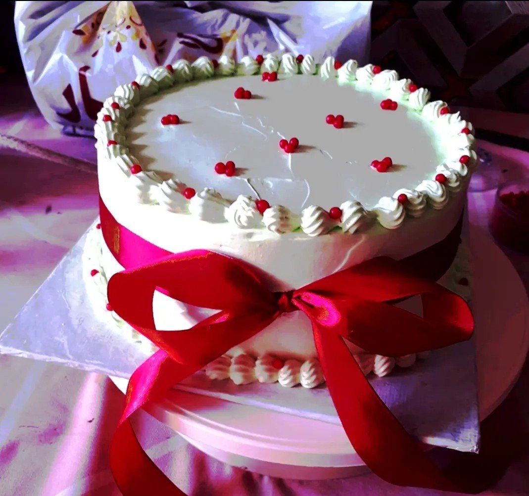 White buttercream cake with a shell border, scattered red hearts, and a red satin ribbon bow