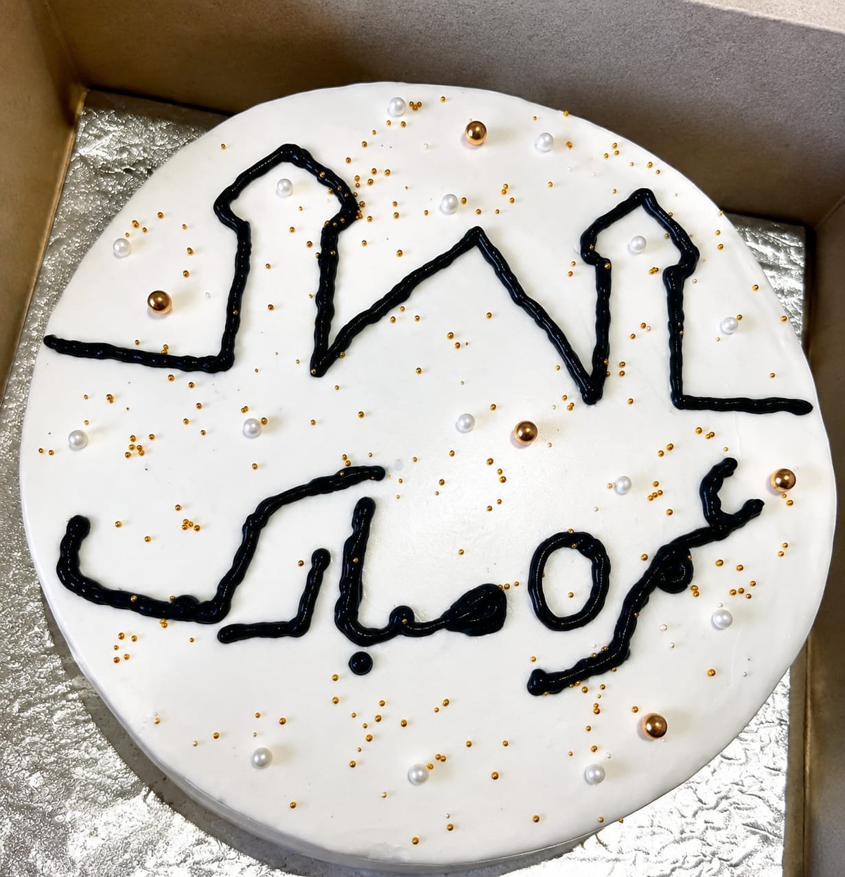 White buttercream cake hand-piped with black Urdu calligraphy and finished with pearls