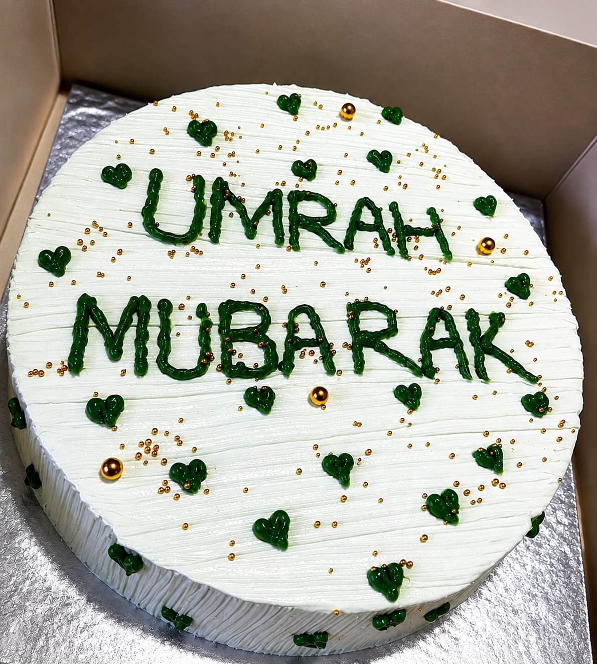 White buttercream cake hand-piped with a green Umrah Mubarak message, hearts, and gold beads